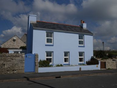 A blue two story house with white framed windows and a stone wall in front at Fisherman's Cottage in Southwell