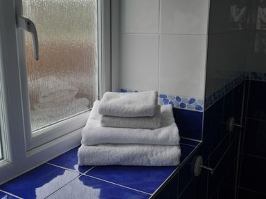A stack of white towels on a blue tiled windowsill in a bathroom at Fisherman's Cottage in Southwell