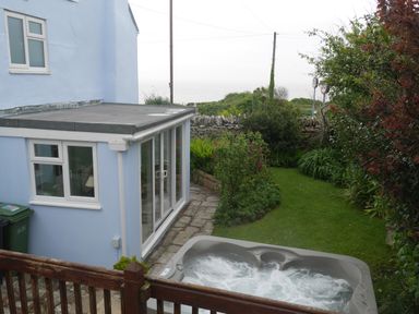 Backyard with a hot tub lawn plants stone wall and light blue house with glass doors at Fisherman's Cottage in Southwell