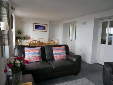 A living room with a black leather sofa and dining table with wooden chairs at Fisherman's Cottage in Southwell