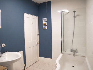 A bathroom with a bathtub and shower, a white door, a sink, and a radiator at Fisherman's Cottage in Southwell