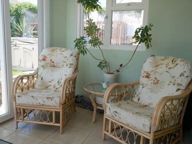 Two wicker armchairs with floral cushions and a round glass table with a potted plant between them in a sunlit room at Fisherman's Cottage in Southwell