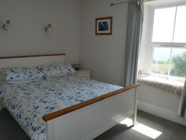 A bedroom with a bed with blue and white floral bedding a bedside table a window with curtains and a framed picture on the wall at Fisherman's Cottage in Southwell
