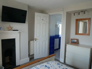 A bedroom with a bed a wall-mounted television a white dresser and an open door showing a bathroom at Fisherman's Cottage in Southwell