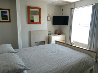 A bedroom with a bed pillows a chest of drawers a wall mirror and a wall mounted tv at Fisherman's Cottage in Southwell