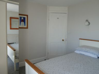 A bedroom with a bed, a door, a wall lamp, a framed picture of a lighthouse, and a full-length mirror at Fisherman's Cottage in Southwell