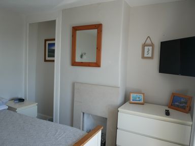 A bedroom with a bed a bedside table a dresser with framed pictures a wall-mounted television and a wooden-framed mirror at Fisherman's Cottage in Southwell