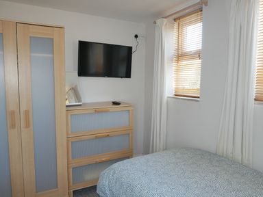 A bedroom with a bed a chest of drawers a wardrobe a wall-mounted TV and two windows with blinds at Fisherman's Cottage in Southwell