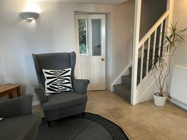 A sitting area with two grey armchairs a pillow a wooden side table a door stairs a potted plant and a radiator at Fishermans Cottage in Southwell