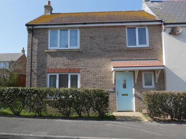 A front view of a two-story brick house with a blue door and hedges at Cliffwalk Cottage in Southwell