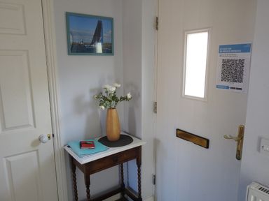 An entrance area with a white door, small wooden table with vase of flowers and documents at Cliffwalk Cottage in Southwell