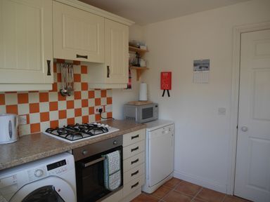A kitchen with checkered orange and white backsplash cabinets countertop oven washing machine microwave and dishwasher at Cliffwalk Cottage in Southwell
