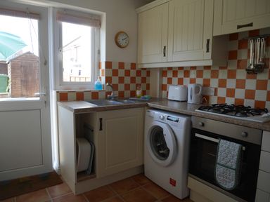 A kitchen with a washing machine oven microwave white cabinets and orange and white tiled walls at Cliffwalk Cottage in Southwell