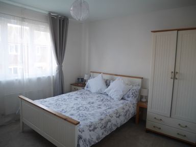 A bedroom with a bed a wardrobe a bedside table and a window with grey curtains at Cliffwalk Cottage in Southwell