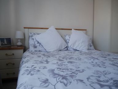 A bed with floral bedspread and pillows and a bedside table with a lamp and picture at Cliffwalk Cottage in Southwell