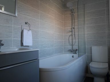 A bathroom with a bathtub shower combination a toilet and a sink cabinet at Cliffwalk Cottage in Southwell