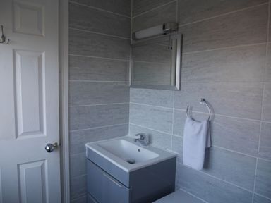 A bathroom sink with a mirror and towel ring on tiled walls at Cliffwalk Cottage in Southwell