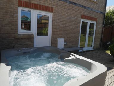 An outdoor hot tub with bubbling water outside a brick house with two white doors and a small bench at Cliffwalk Cottage in Southwell