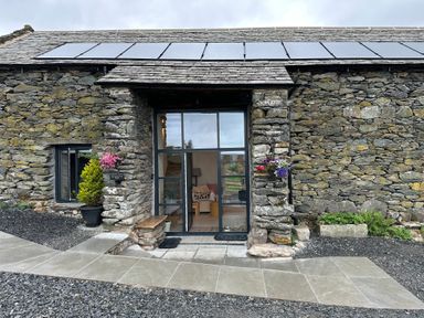 Stone barn with glass door entrance flowers in pots and solar panels on roof at Meadow Syke Barn in Bampton Cumbria