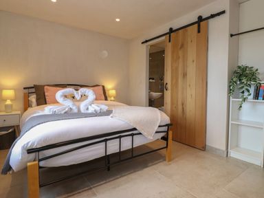 A bedroom with a double bed with towels shaped like swans and a wooden sliding door leading to a bathroom at Meadow Syke Barn in Bampton Cumbria