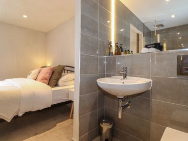 A bedroom with a bed and pillows next to a bathroom sink and mirror at Meadow Syke Barn in Bampton Cumbria