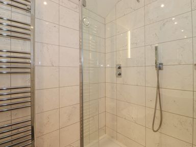 A shower area with a handheld showerhead and controls tiled walls and a chrome towel radiator at Meadow Syke Barn in Bampton Cumbria