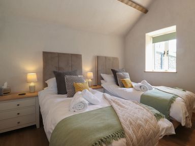 A bedroom with two single beds bedside tables lamps and a window at Meadow Syke Barn in Bampton Cumbria