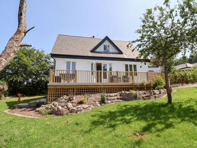 A house with a wooden deck and garden with rocks and trees at Melbecks in Abergele