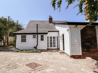 An exterior view of a white house with a stone patio and surrounding trees at Melbecks in Abergele
