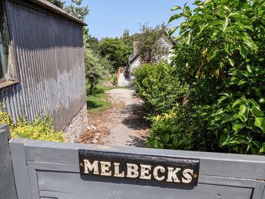 A gravel path leading to a white house with bushes and trees on both sides at Melbecks in Abergele