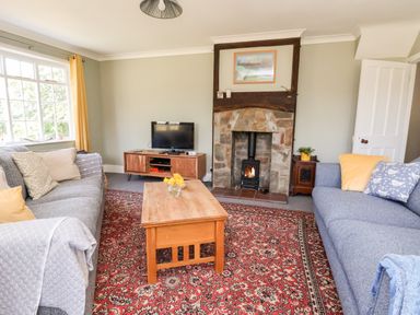 A living room with two sofas a wooden coffee table a red patterned rug and a stone fireplace with a wood stove at Melbecks in Abergele