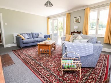 A living room with two sofas a wooden coffee table a red patterned rug yellow curtains and a small wooden side table at Melbecks Abergele