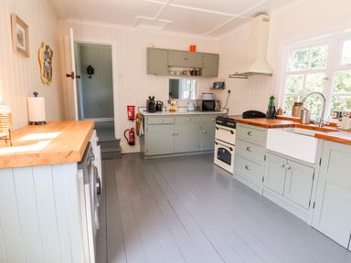 A kitchen with gray cabinets wooden countertops a white farmhouse sink stove microwave and a window at Melbecks in Abergele