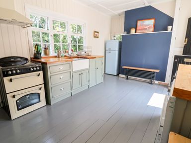A kitchen with a stove sink cabinets window refrigerator and a bench against a blue wall at Melbecks in Abergele