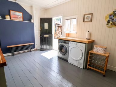 A laundry room with a washing machine and dryer under a wooden countertop and an open black door at Melbecks in Abergele