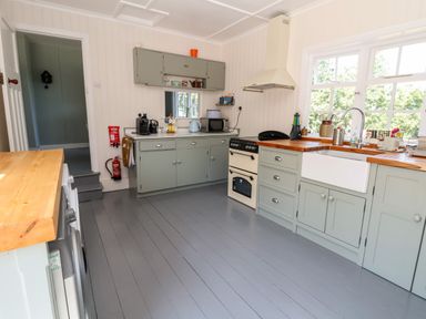 A kitchen with grey cabinets wooden countertops a stove a white sink and appliances next to a window at Melbecks Abergele