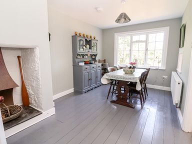 A dining room with a wooden table and chairs a grey cabinet and a bay window at Melbecks in Abergele