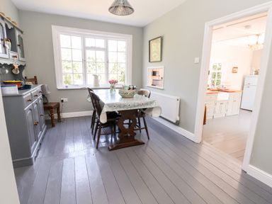 A dining room with a wooden table and chairs next to a window and a gray cabinet with dishes at Melbecks in Abergele