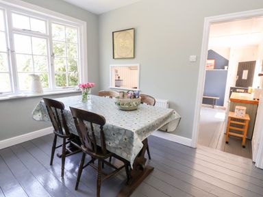 A dining room with a table covered by a tablecloth and wooden chairs near a window at Melbecks in Abergele
