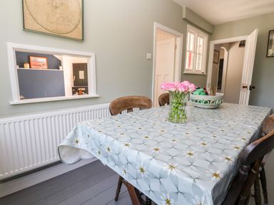 A dining room with a table covered by a patterned tablecloth with a vase of pink flowers and a basket on it at Melbecks Abergele