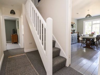 A hallway with carpeted stairs and a patterned rug leading to a dining room with a wooden table and chairs at Melbecks in Abergele