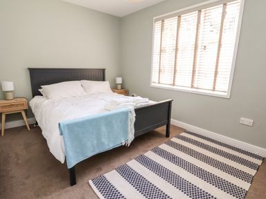 A bedroom with a bed with white bedding and blue throw a striped rug and two bedside tables at Melbecks Abergele