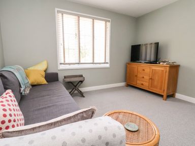 A sitting room with a gray sofa cushions a wooden cabinet with a television and a small round wicker table at Melbecks in Abergele