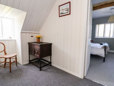 A small corner with a wooden chair and a dark wooden cabinet with a vase of yellow flowers and a view into a bedroom at Melbecks in Abergele