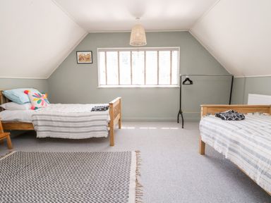 A bedroom with two single wooden beds, a window with blinds, a rug, a clothes rack with hangers, and a framed picture on the wall at Melbecks in Abergele