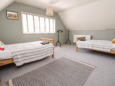 A bedroom with two single beds a patterned rug and a window with blinds at Melbecks in Abergele