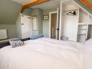 A bedroom with a bed white bedding towels on footboard a mirror and an open closet at Melbecks in Abergele
