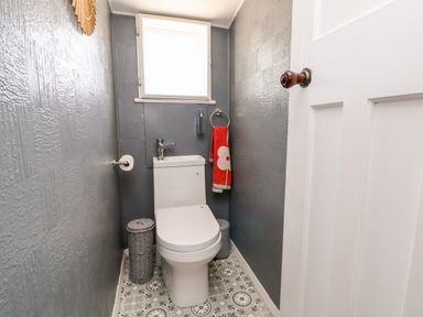 A small bathroom with a toilet a window a red towel on a ring and a wicker bin at Melbecks in Abergele