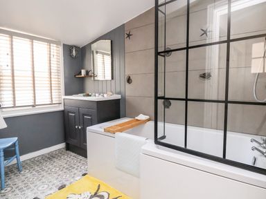 A bathroom with a bathtub with a glass screen and a sink with a mirror above at Melbecks in Abergele