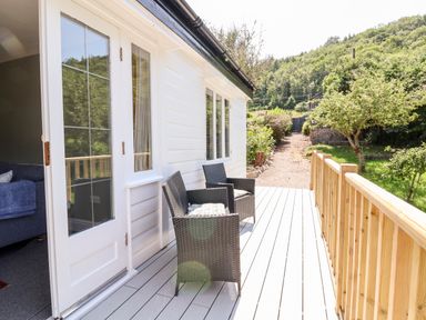 A porch with two chairs and a railing outside a white house with a door open to a living room at Melbecks in Abergele